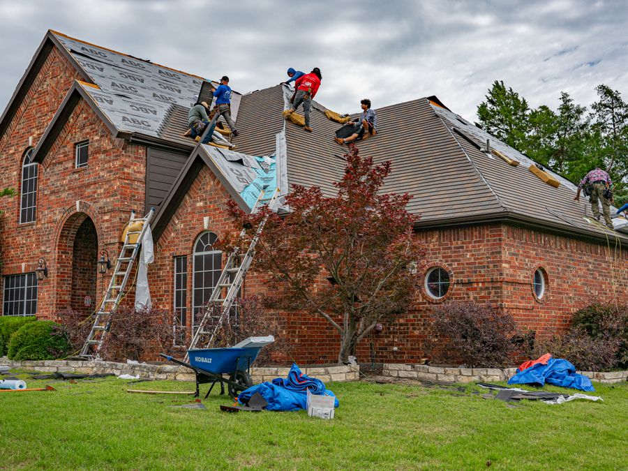 A roofing crew working on the shingles of a brick house